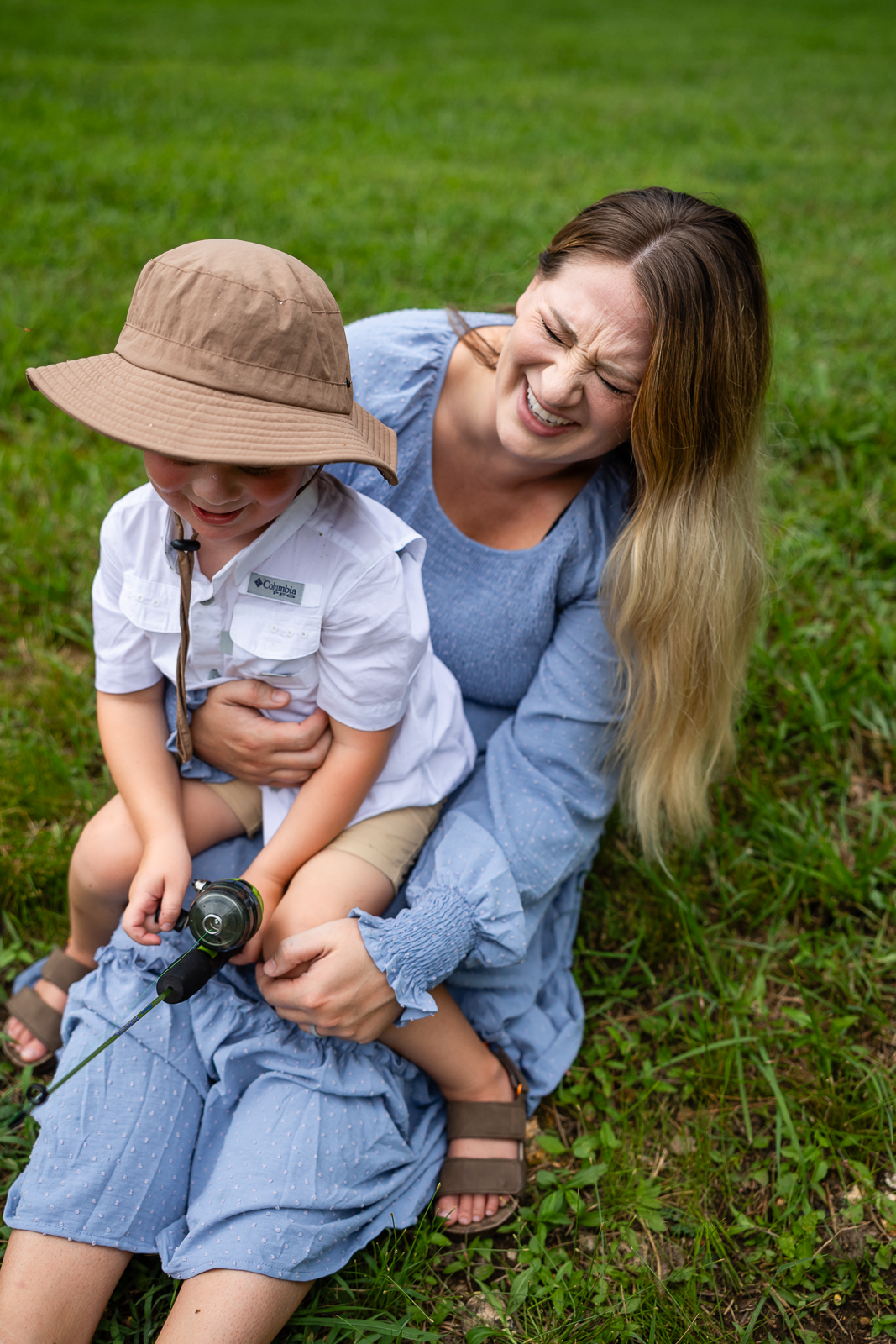 Boy sitting in moms lap while they fish and mom is laughing really hard a something the boy said.