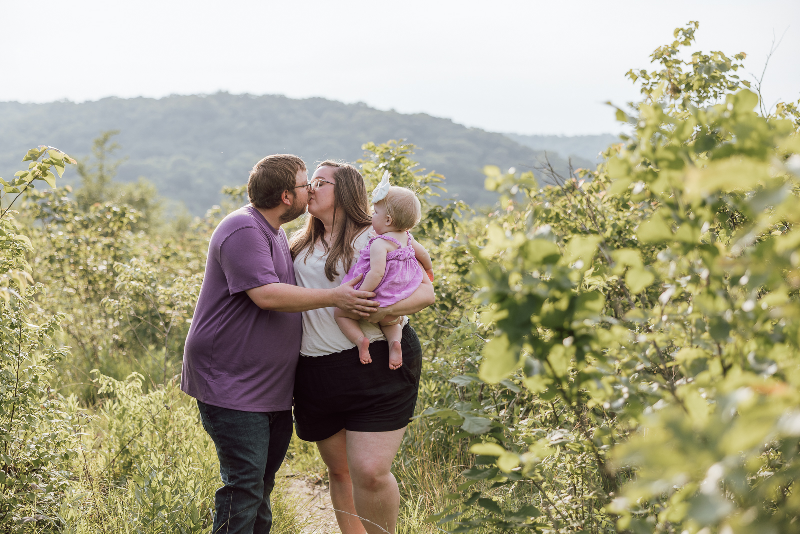 Family of three smiling together outdoors during a portrait session in De Soto, Missouri.