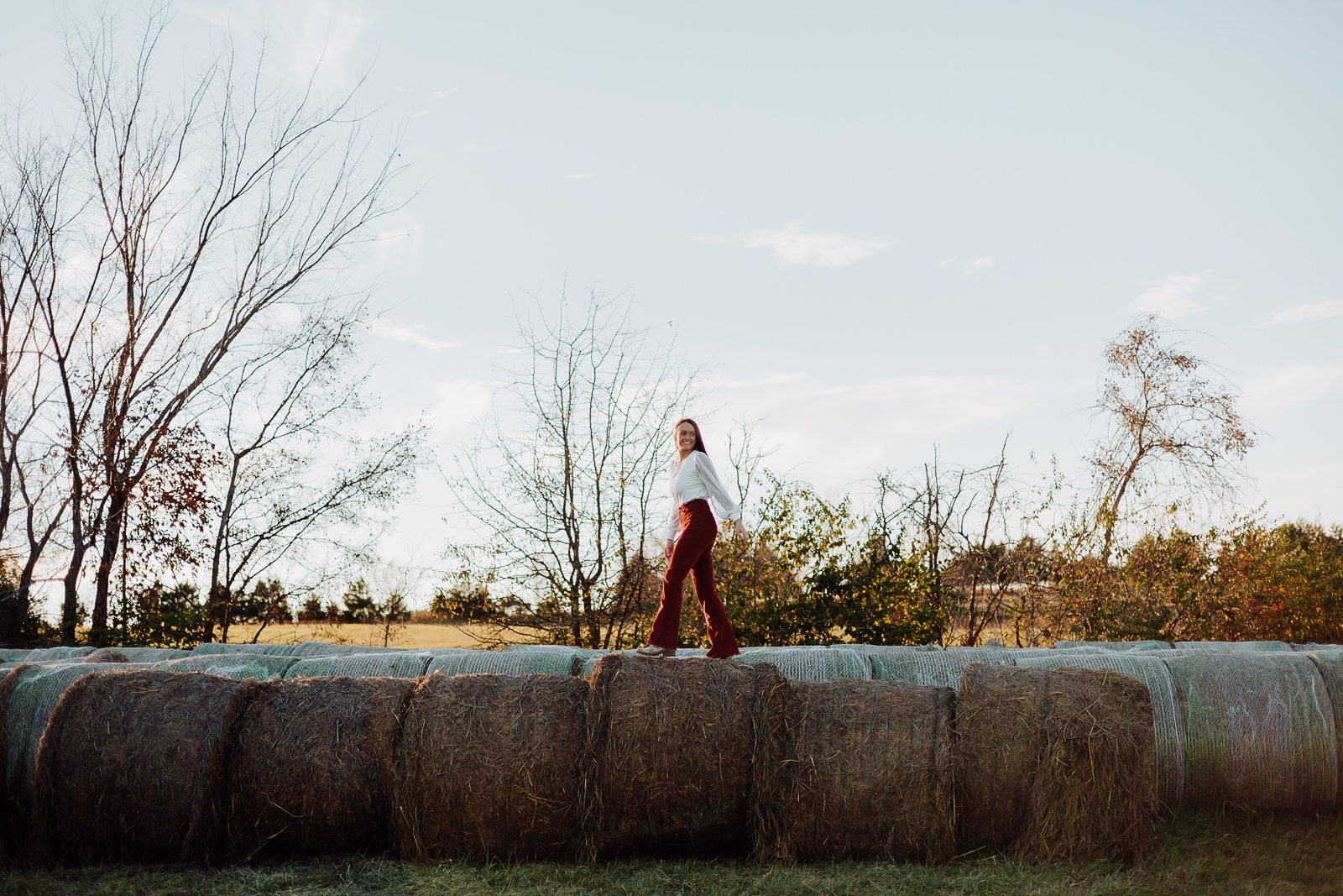 High school senior girl walking across hay bales in Farmington, Missouri during her fall senior portrait session with Jennifer Mosier Photography.
