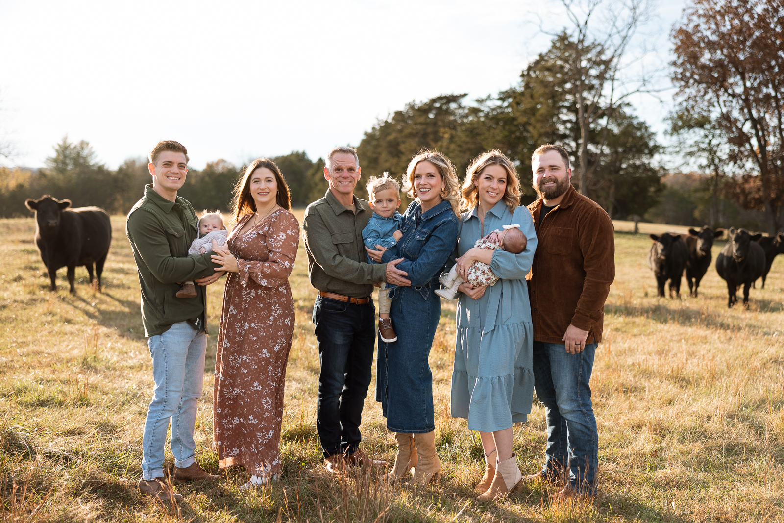 Extended family standing together in a field at sunset with cows in the background, smiling during a portrait session in De Soto, Missouri.