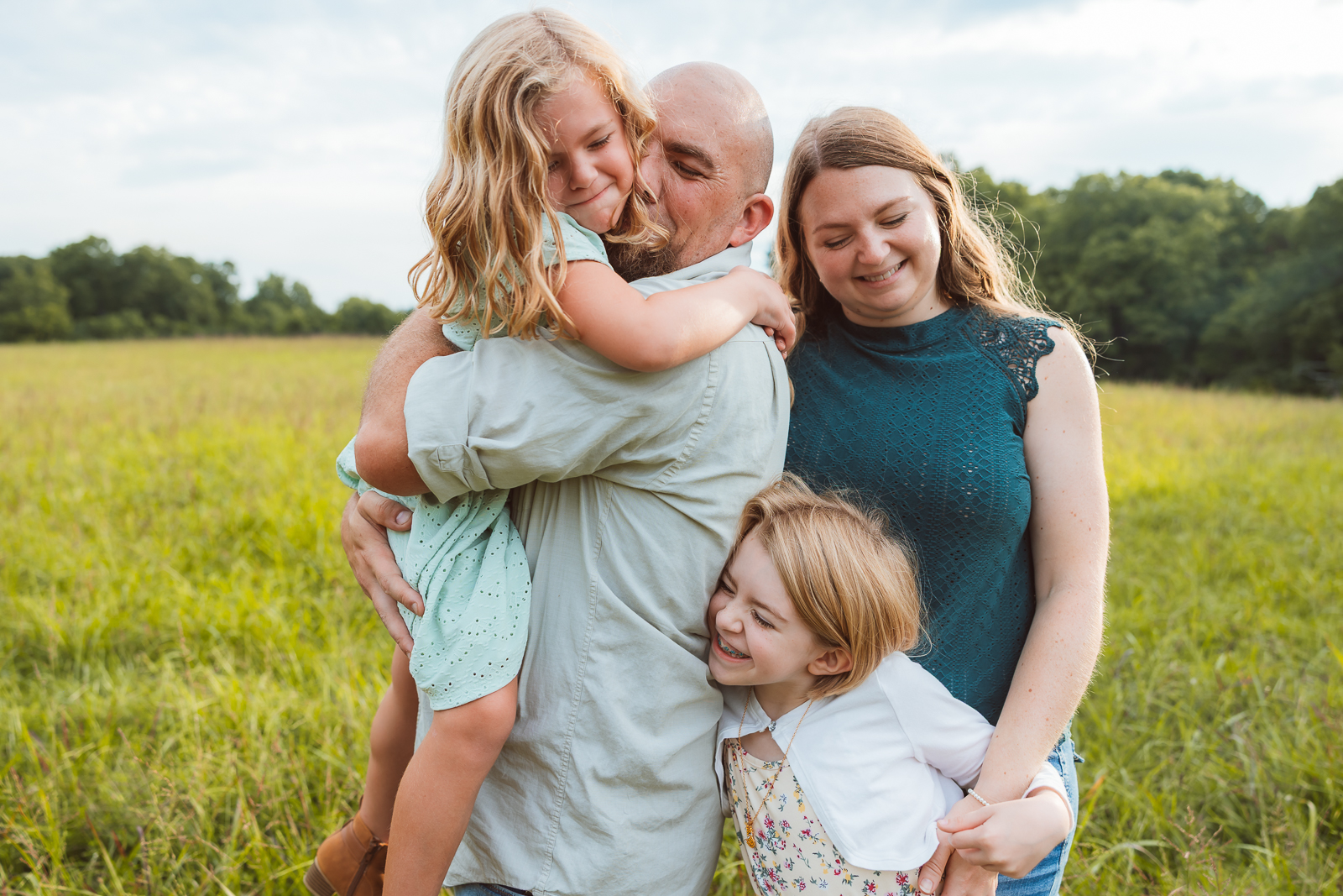 Family portrait taken outdoors in De Soto, Missouri taken by Jennifer Mosier, showing parents with their two young children laughing together in a field.