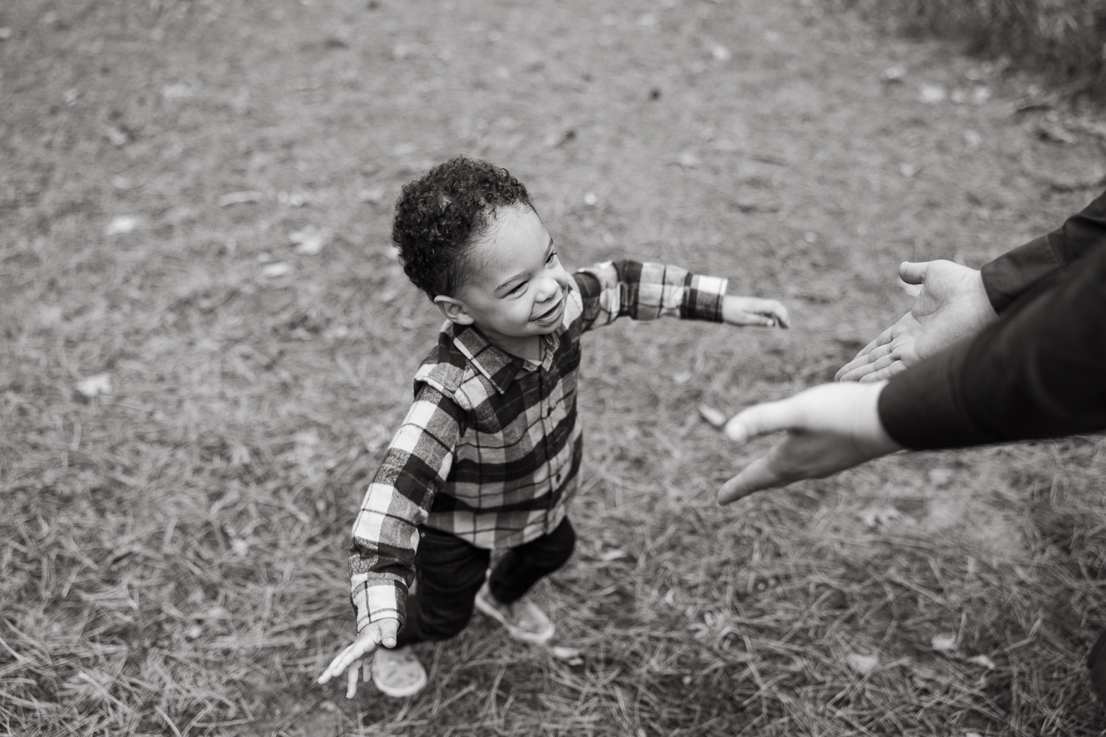 Black and white portrait of a young boy running toward his dad outside, capturing an emotional and candid moment filled with connection and joy.